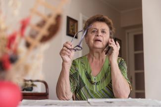 Image of person eyeglasses in right hand and holding a mobile phone near their ear